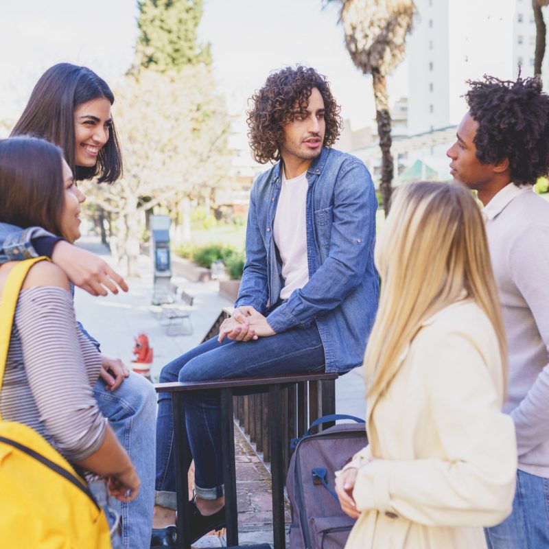 Multi-ethnic group of friends gathered in the street leaning on a railing. Young people having fun together.